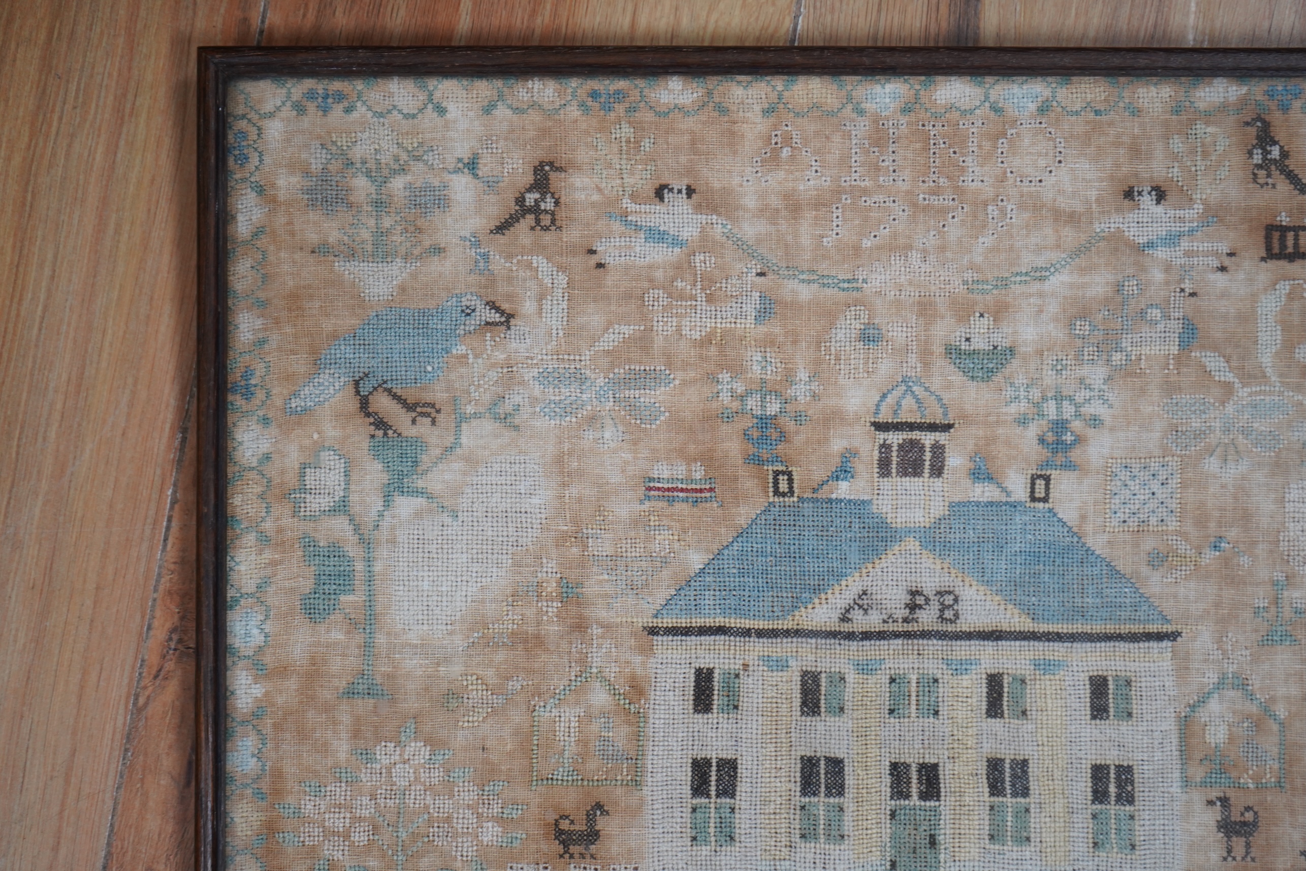 A framed 18th century sampler, dated 1779 by SS., worked in fine cross stitch with motifs of angels, figures, flowers, trees birds a fox and a stag surrounding a house with initials APB. 39cm x 37.5cm. Condition - the em